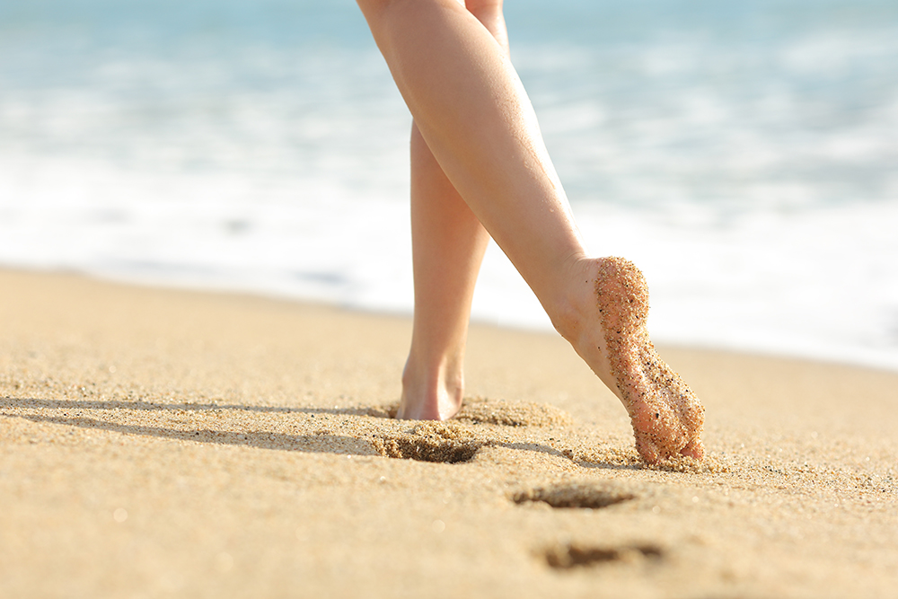 Woman legs and feet walking on the sand of the beach with the sea water in the background